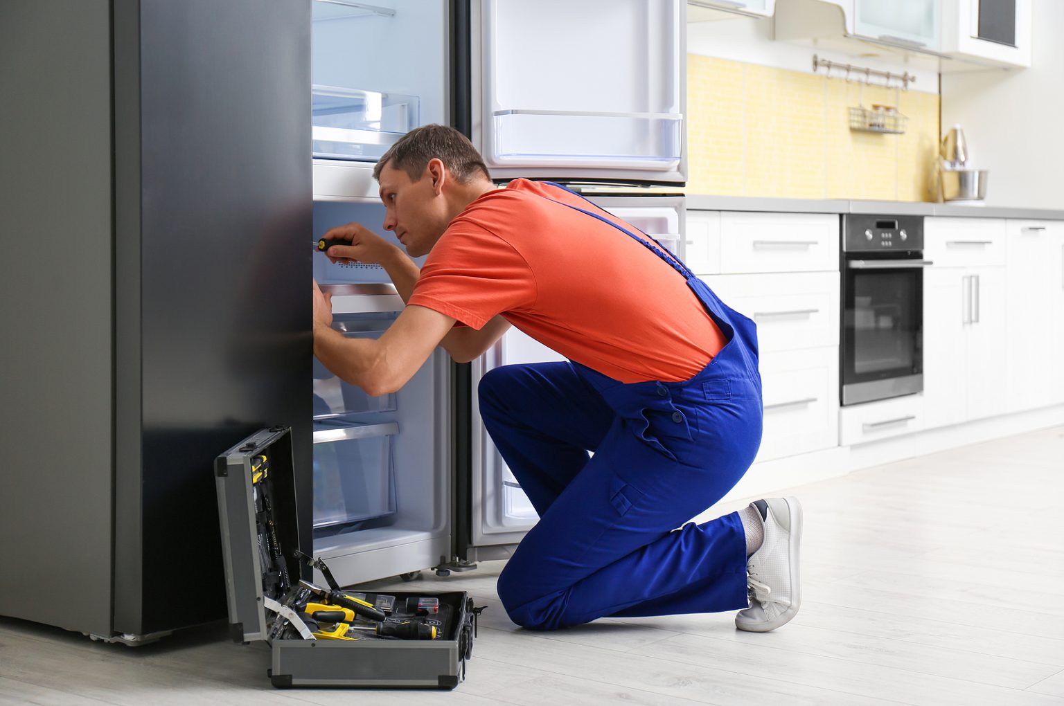 Male Technician With Screwdriver Repairing Refrigerator in Kitchen 1536x1020 1